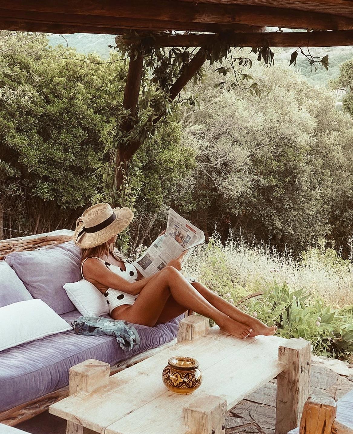 Femme assise sur un fauteuil entrain de lire le journal aux Oliviers de Palombaggia en Corse-du-Sud. 